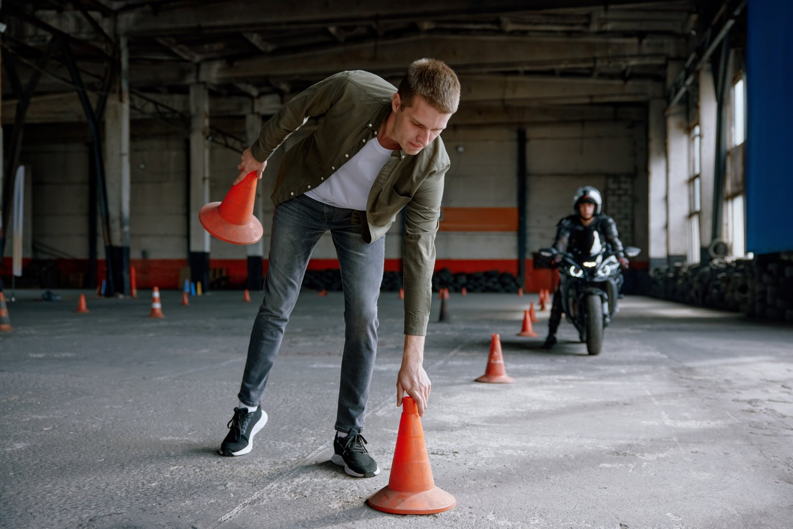 Motorbike driving school lesson with instructor putting cone on track front of student. Indoor motodrome training center